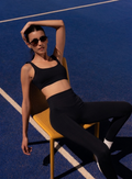 Woman in black athletic wear sitting on a yellow chair against a blue background