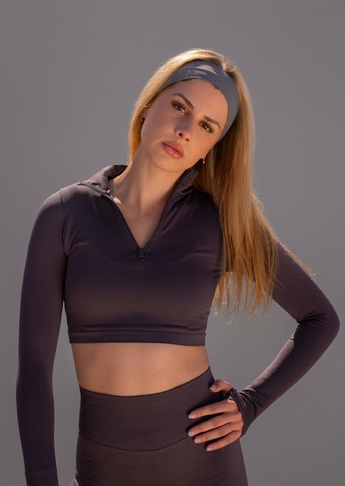 Woman with headband wearing a dark athletic outfit on a gray background