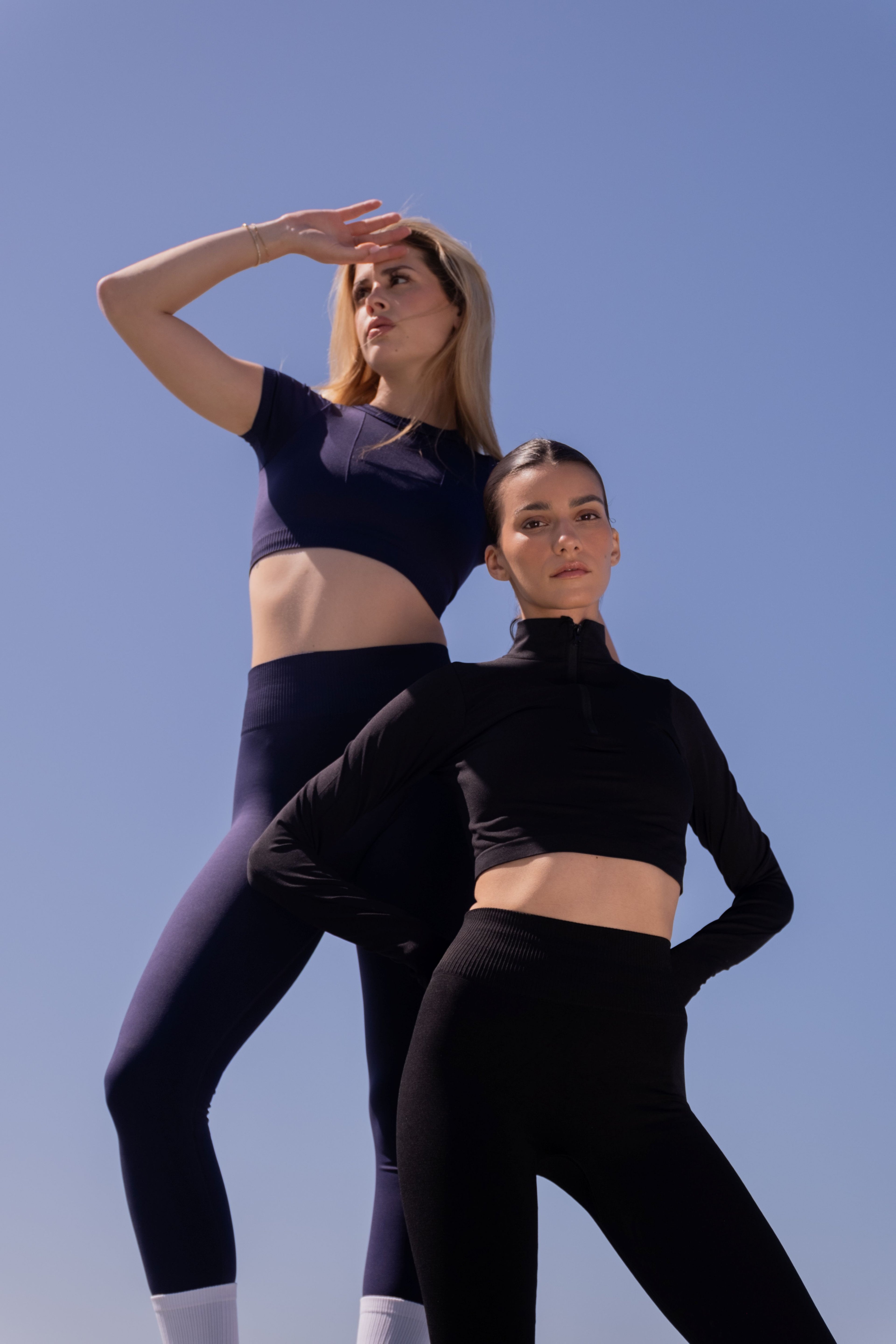 Two women in athletic wear standing against a clear blue sky.
