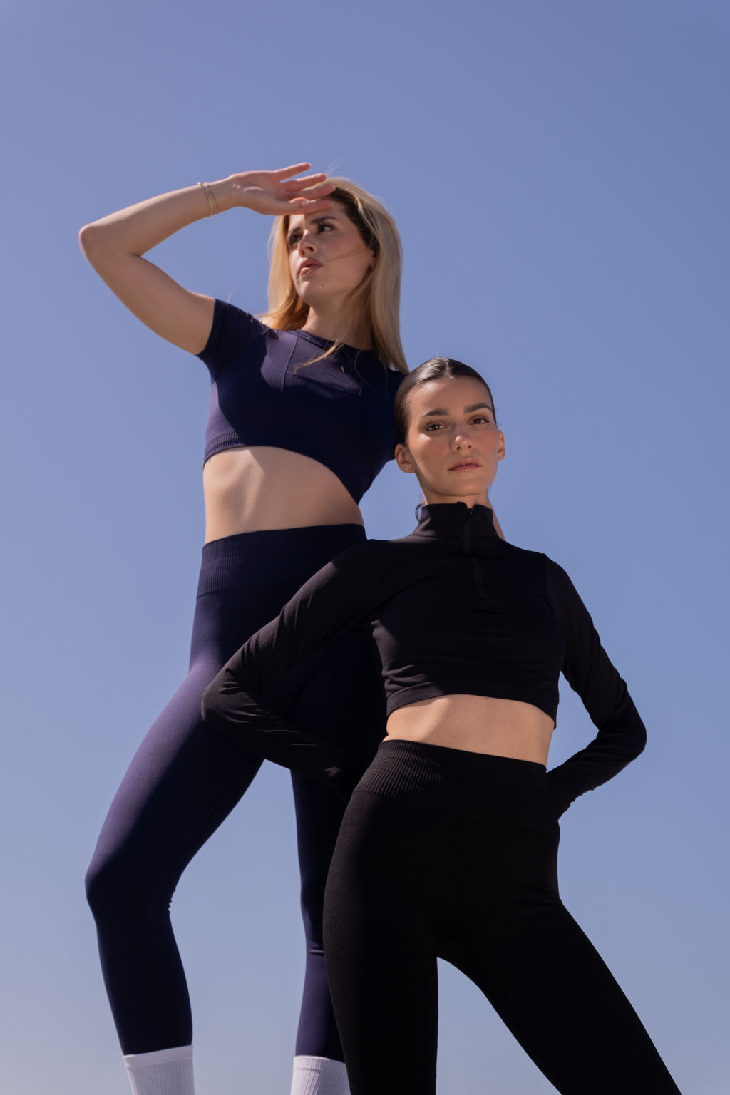Two women in athletic wear standing against a clear blue sky.