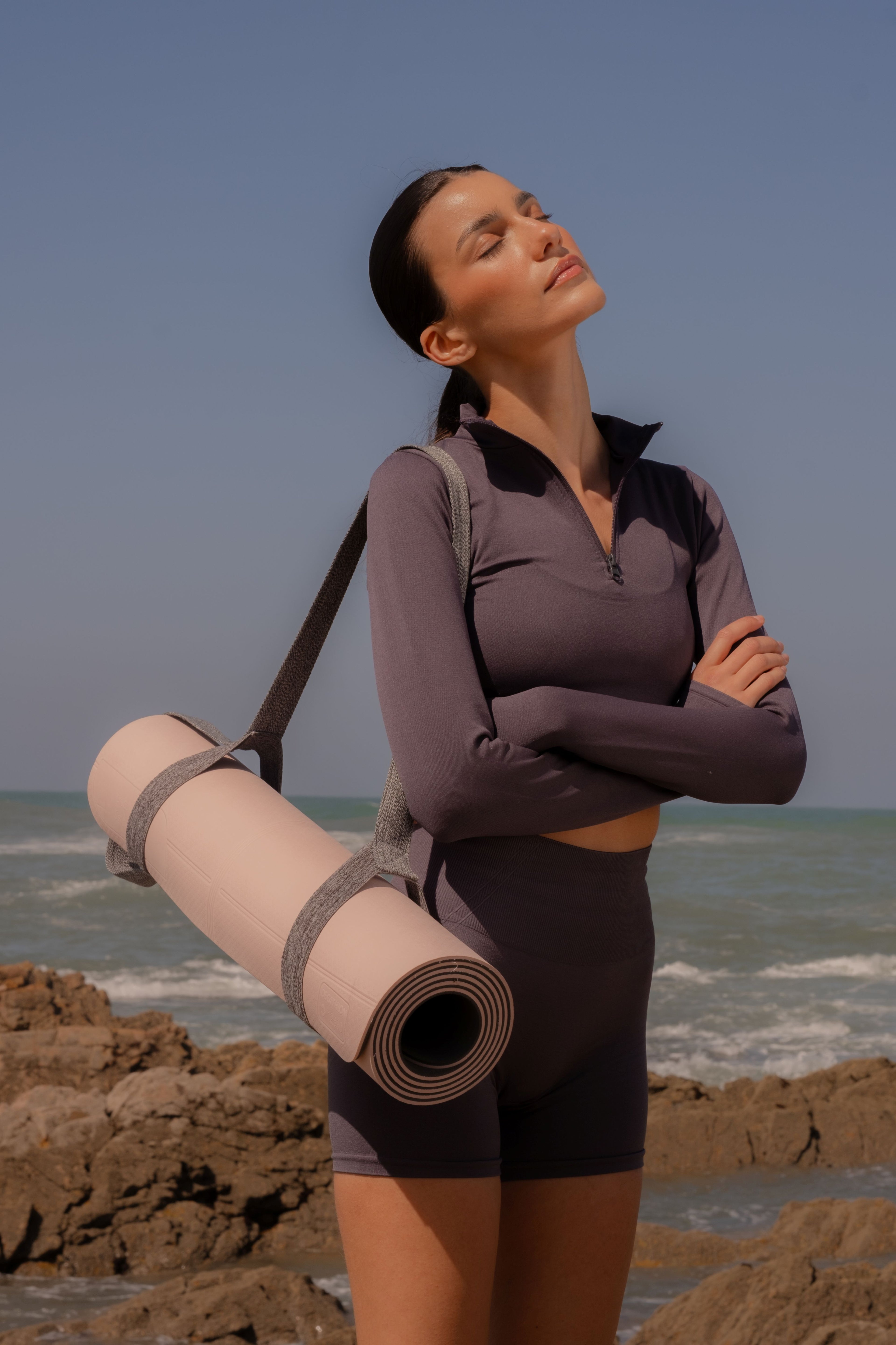 Woman holding a yoga mat on a rocky beach with ocean and sky in the background
