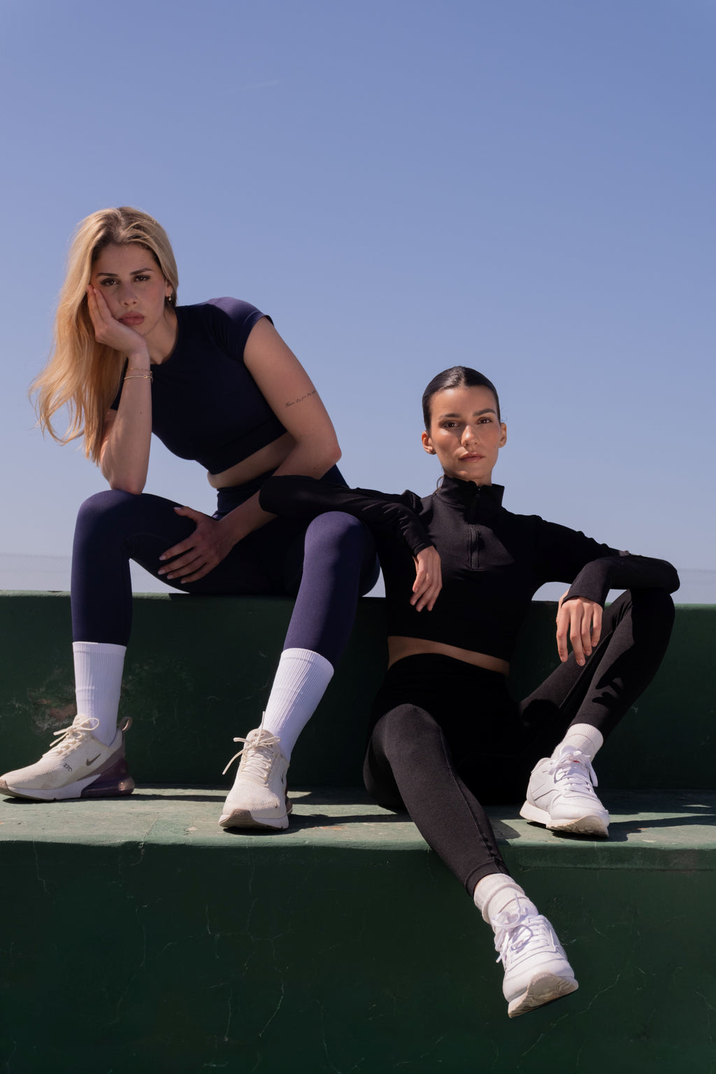 Two women sitting on a ledge against a clear blue sky