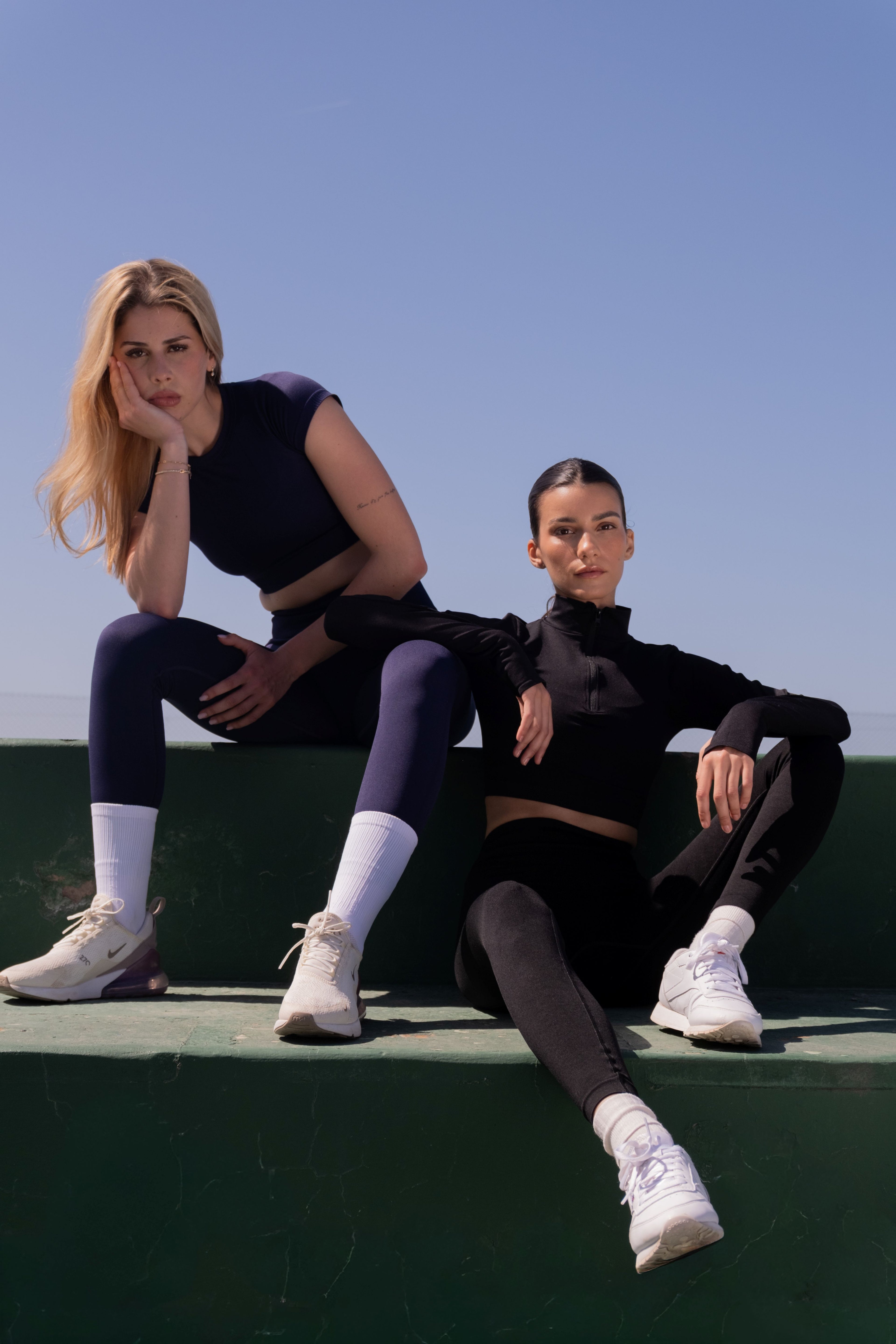 Two women sitting on a ledge against a clear blue sky