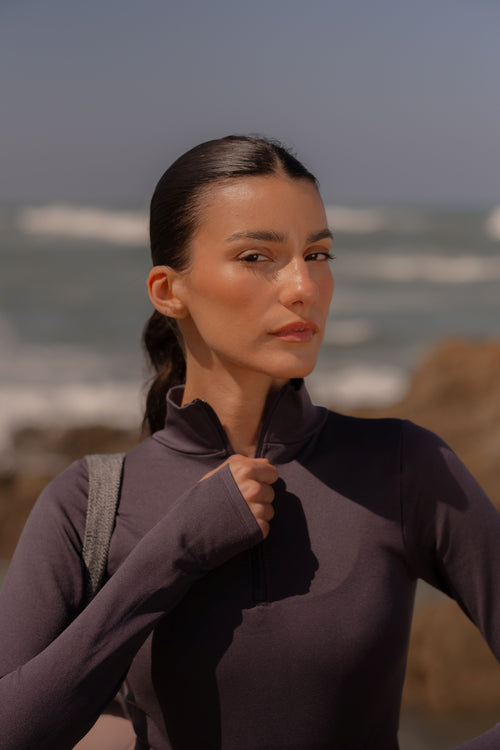 Woman in a purple outfit standing on a rocky beach with ocean waves in the background