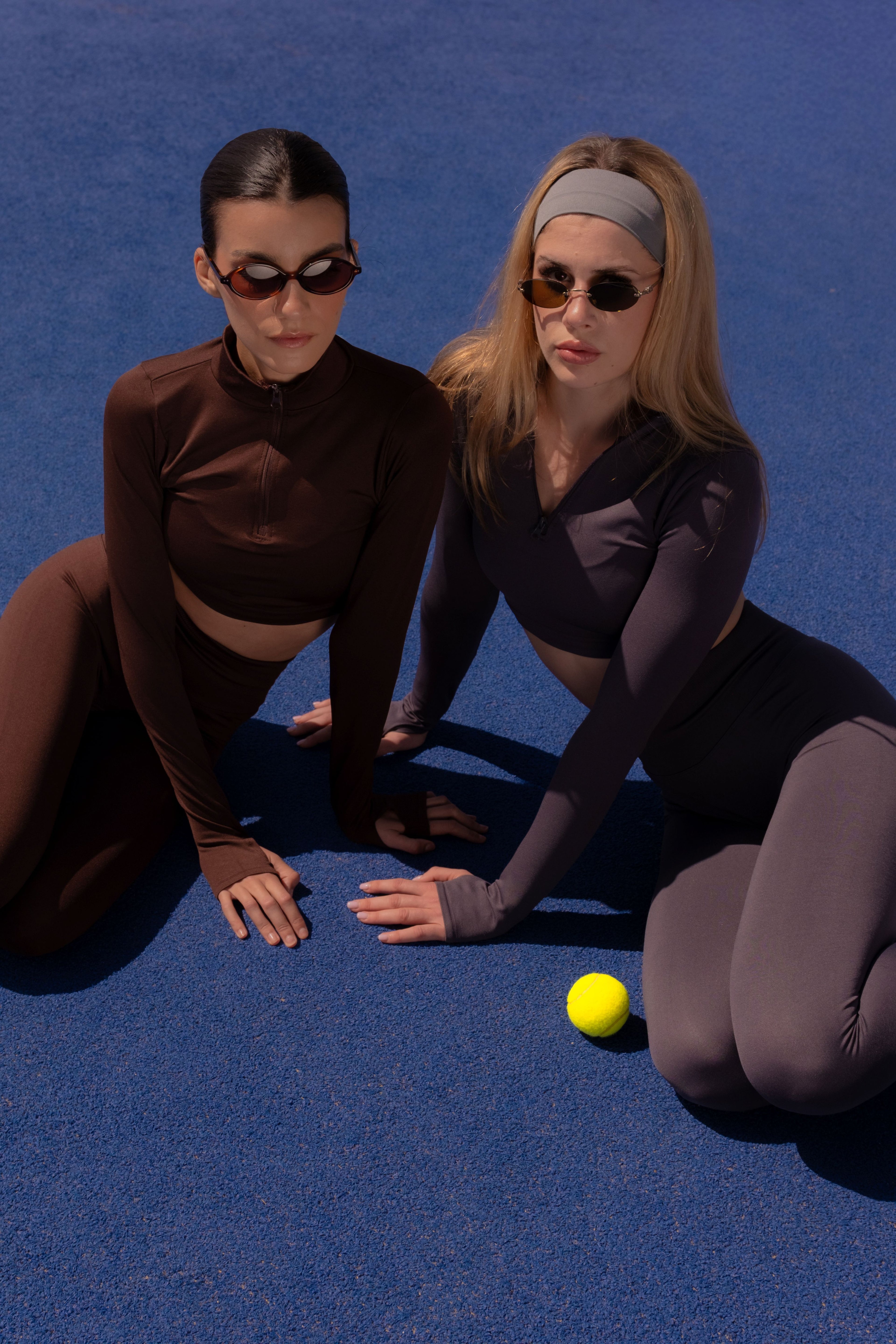 Two women in matching outfits with sunglasses and a yellow ball on a blue background