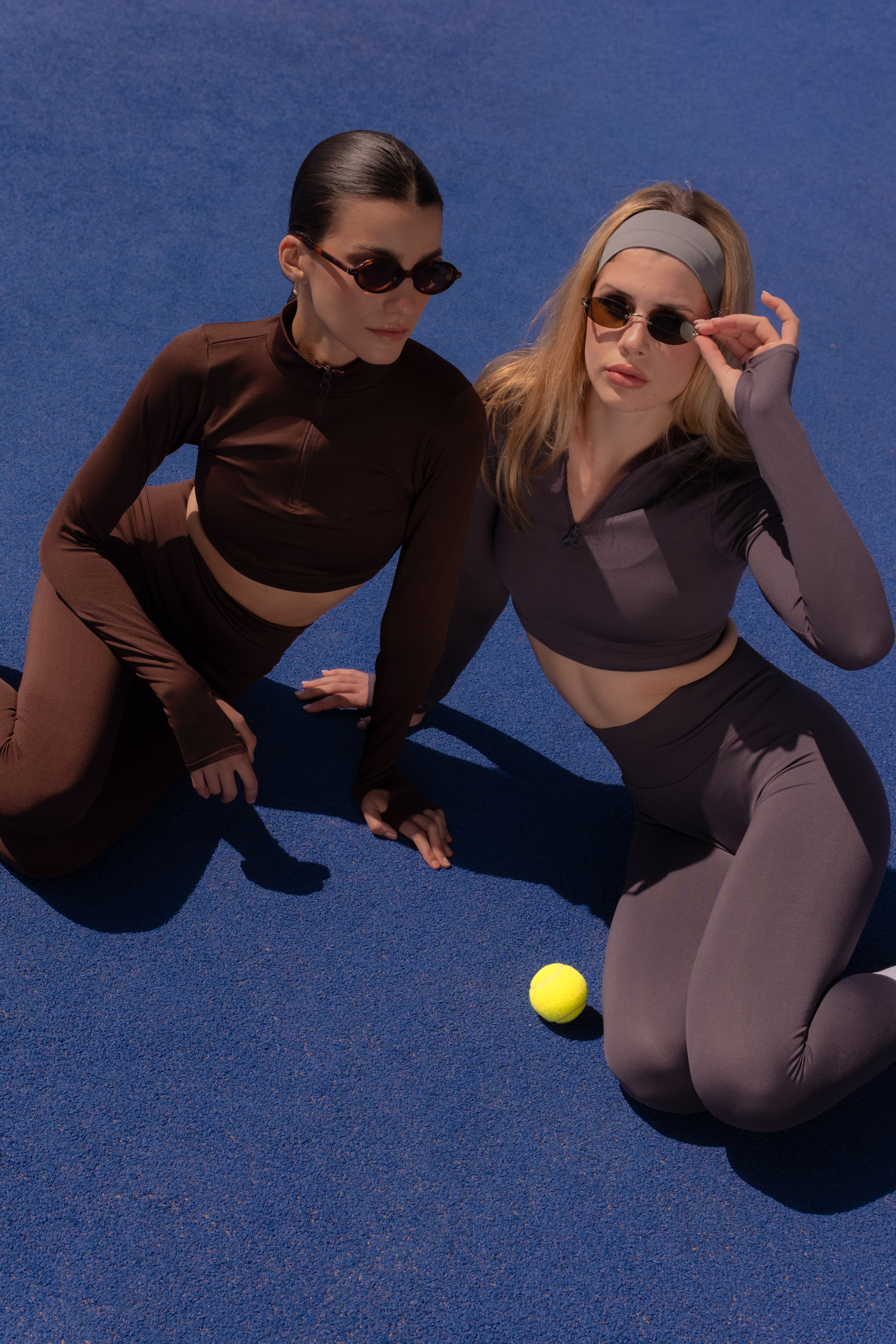 Two women in matching outfits kneeling on a blue surface with a yellow ball between them.